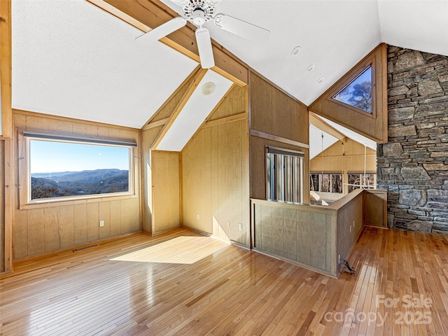 additional living space with a mountain view, lofted ceiling with beams, light hardwood / wood-style flooring, and wood walls