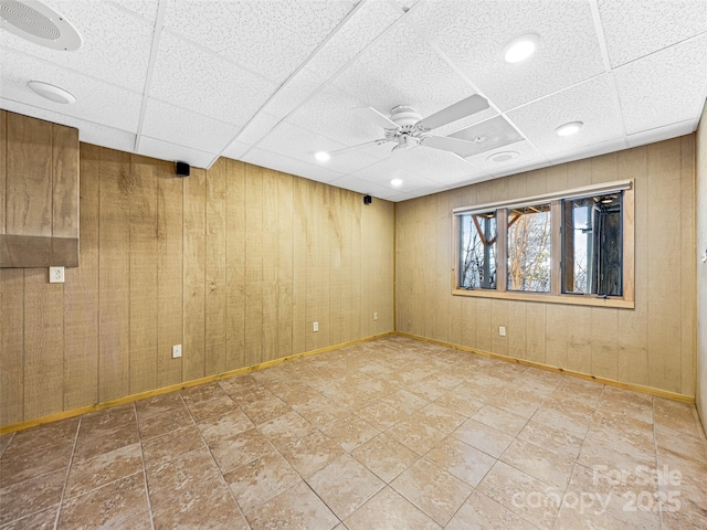 empty room with ceiling fan, wooden walls, and a paneled ceiling