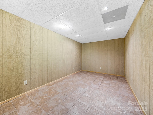 empty room featuring a drop ceiling and wood walls