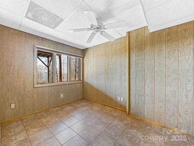 unfurnished room with ceiling fan, wooden walls, and a paneled ceiling