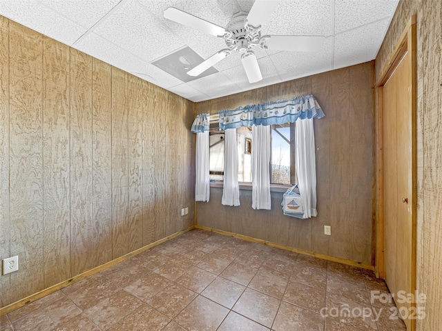 empty room with a paneled ceiling, ceiling fan, and wood walls