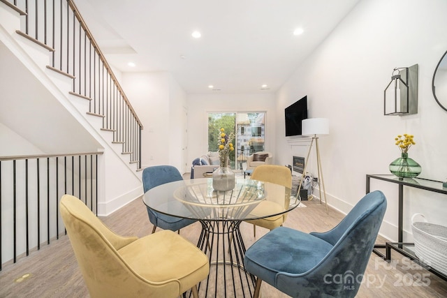 dining area featuring recessed lighting, baseboards, stairway, light wood-type flooring, and a glass covered fireplace