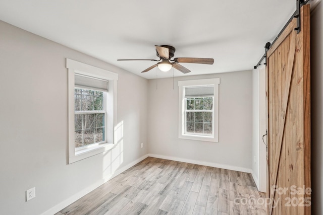 empty room featuring a barn door, a wealth of natural light, ceiling fan, and light hardwood / wood-style flooring