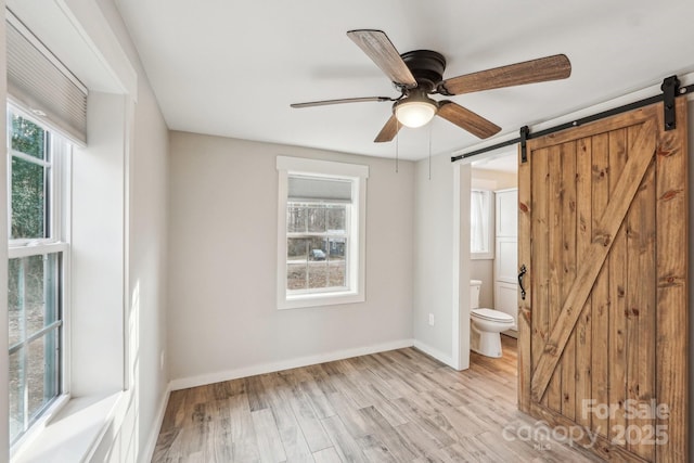 empty room featuring ceiling fan, a barn door, and light hardwood / wood-style flooring