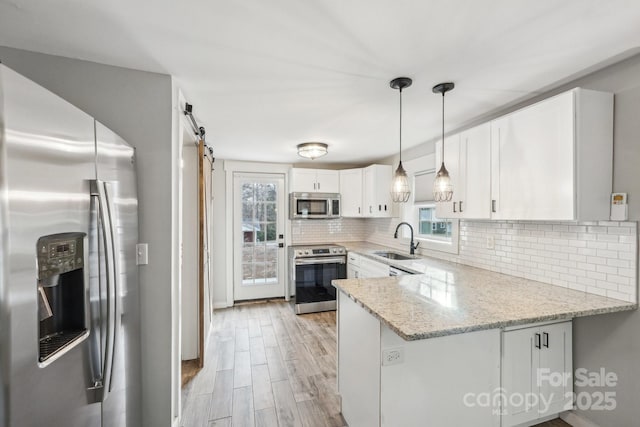 kitchen featuring sink, white cabinetry, stainless steel appliances, light stone counters, and a barn door