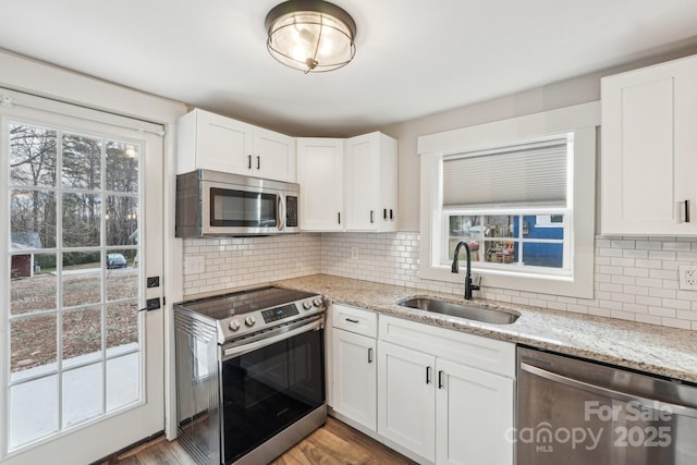 kitchen with sink, white cabinets, stainless steel appliances, light stone countertops, and backsplash