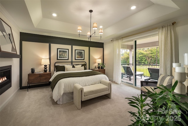 bedroom featuring access to outside, a tray ceiling, light colored carpet, and a glass covered fireplace