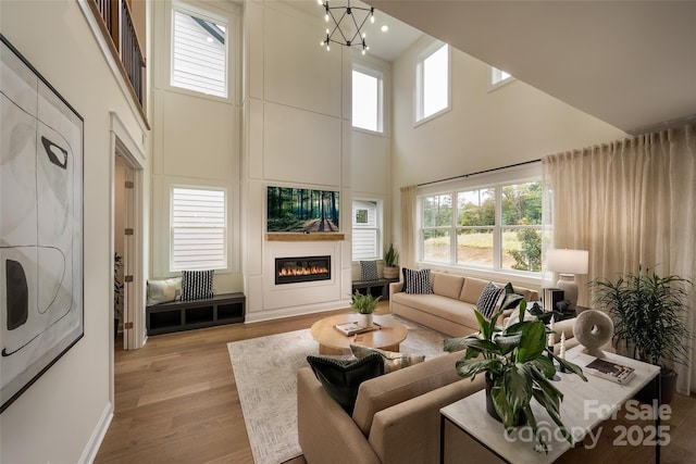 living area featuring a large fireplace, light wood finished floors, a high ceiling, and a notable chandelier