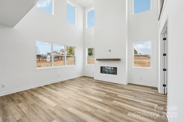 604 Hyder Trl, Tega Cay, SC 29708 - unfurnished living room featuring a high ceiling, light wood-type flooring, a glass covered fireplace, and baseboards
