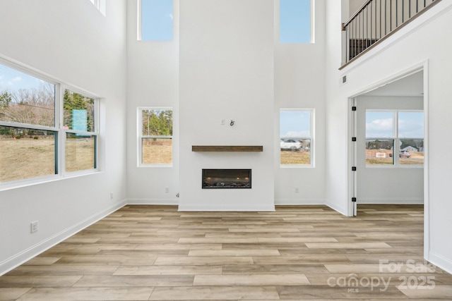 604 Hyder Trl, Tega Cay, SC 29708 - unfurnished living room with a high ceiling, light wood-type flooring, healthy amount of natural light, a fireplace, and baseboards