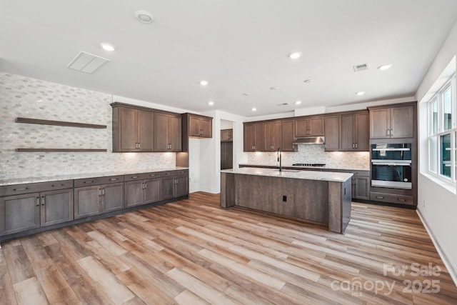 604 Hyder Trl, Tega Cay, SC 29708 - kitchen with under cabinet range hood, appliances with stainless steel finishes, backsplash, light wood-style flooring, and recessed lighting