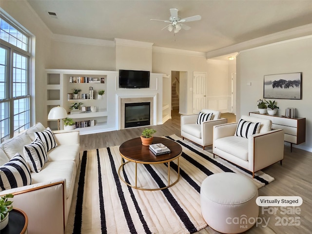 living room with ceiling fan, built in features, crown molding, and light hardwood / wood-style flooring