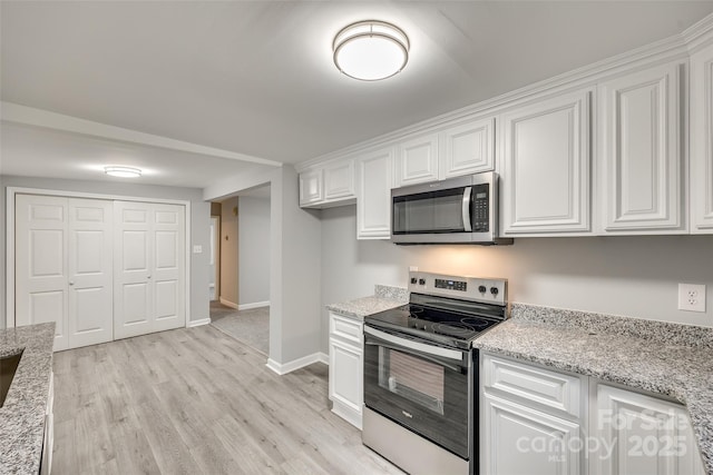 kitchen with light stone countertops, white cabinetry, stainless steel appliances, and light wood-type flooring