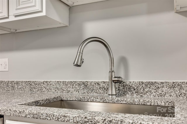 room details featuring white cabinets, sink, and light stone counters