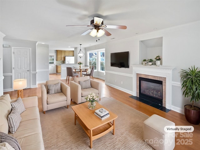 living room featuring ceiling fan, crown molding, light hardwood / wood-style flooring, and a tiled fireplace