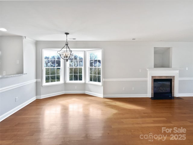 unfurnished living room featuring a notable chandelier, a tile fireplace, ornamental molding, and hardwood / wood-style flooring