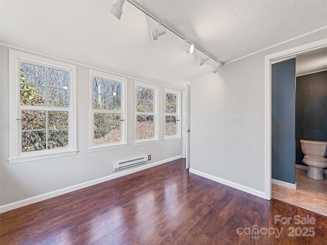 spare room featuring track lighting, a baseboard heating unit, dark wood-type flooring, and a textured ceiling