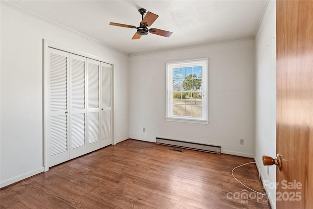 unfurnished bedroom with ceiling fan, a closet, wood-type flooring, crown molding, and baseboard heating