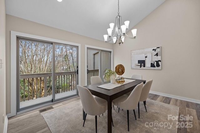 dining space featuring baseboards, visible vents, lofted ceiling, wood finished floors, and an inviting chandelier