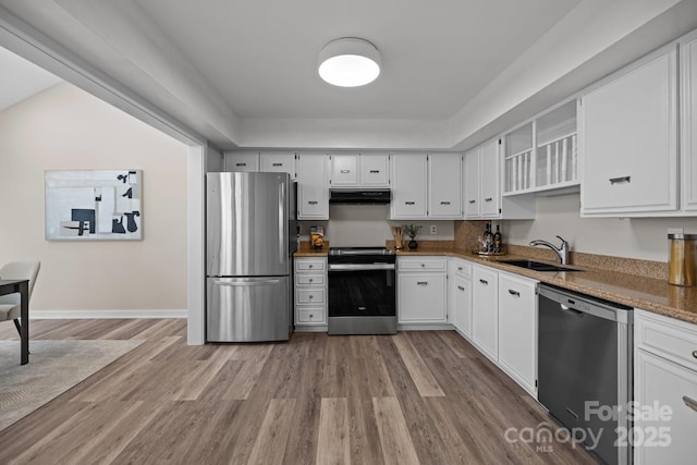 kitchen with light wood finished floors, appliances with stainless steel finishes, white cabinets, a sink, and under cabinet range hood