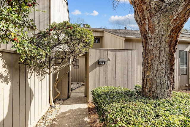 view of exterior entry featuring a shingled roof and fence