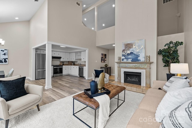 living room with baseboards, visible vents, a tiled fireplace, light wood-style flooring, and recessed lighting