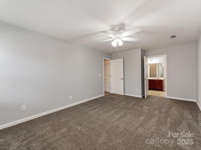 unfurnished bedroom featuring ceiling fan, dark carpet, and ensuite bath