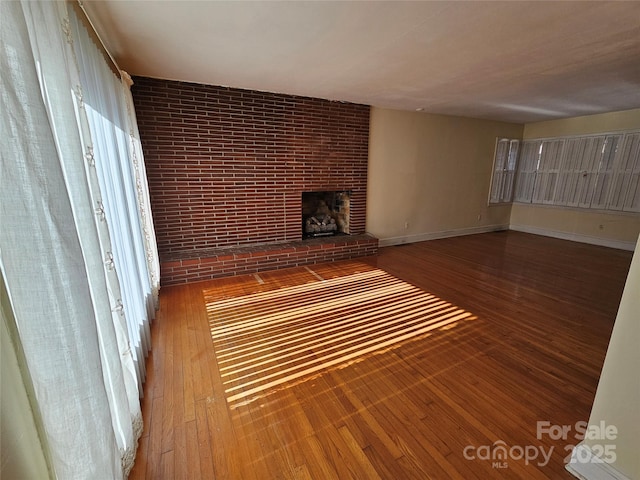 unfurnished living room featuring wood-type flooring, a fireplace, and brick wall