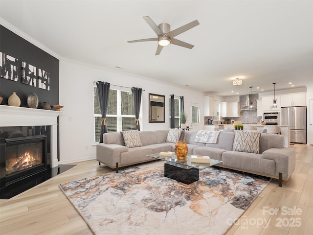 living room featuring light wood-type flooring, ceiling fan, and ornamental molding