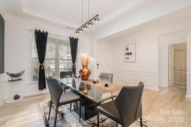 dining space with a tray ceiling, ornamental molding, and light hardwood / wood-style floors