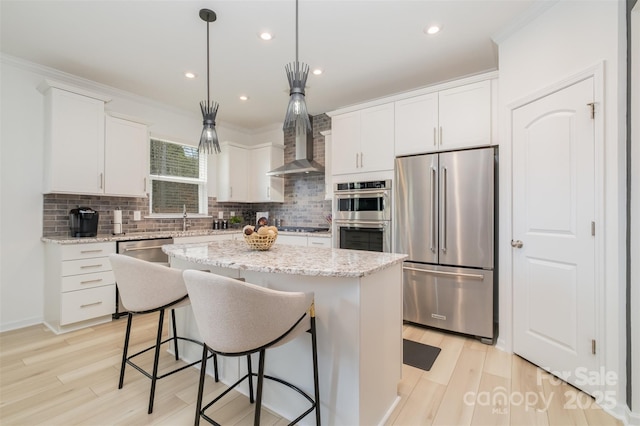 kitchen featuring white cabinets, a kitchen island, wall chimney range hood, stainless steel appliances, and hanging light fixtures