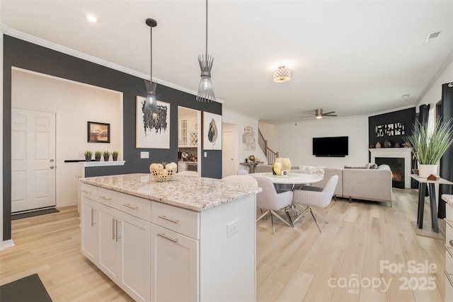 kitchen with pendant lighting, a center island, white cabinetry, ceiling fan, and light stone counters