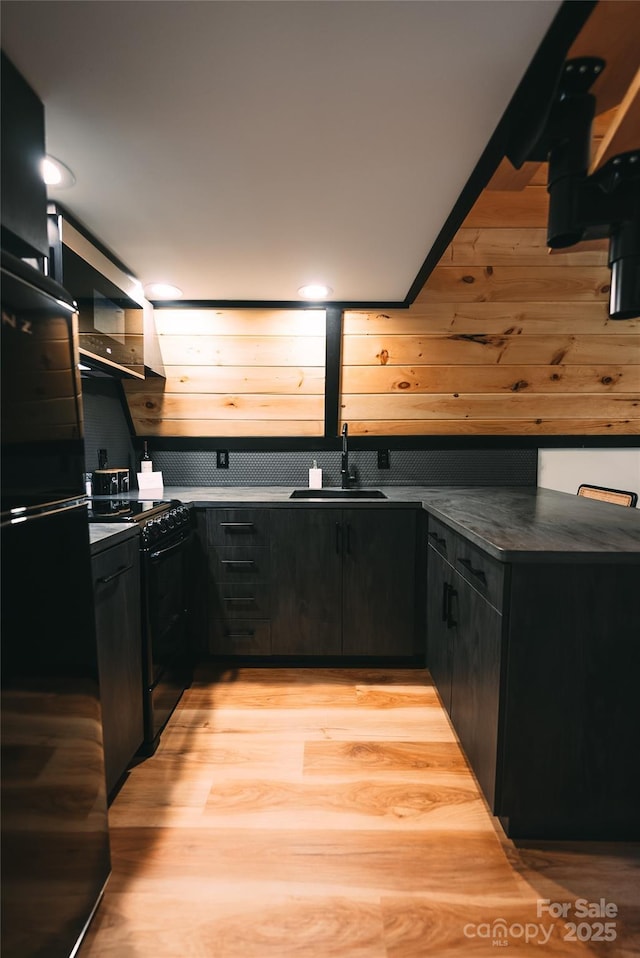 kitchen with black appliances, light wood-type flooring, wooden walls, and sink