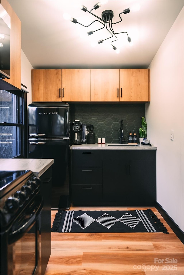 kitchen with wood-type flooring, light brown cabinets, sink, backsplash, and black appliances