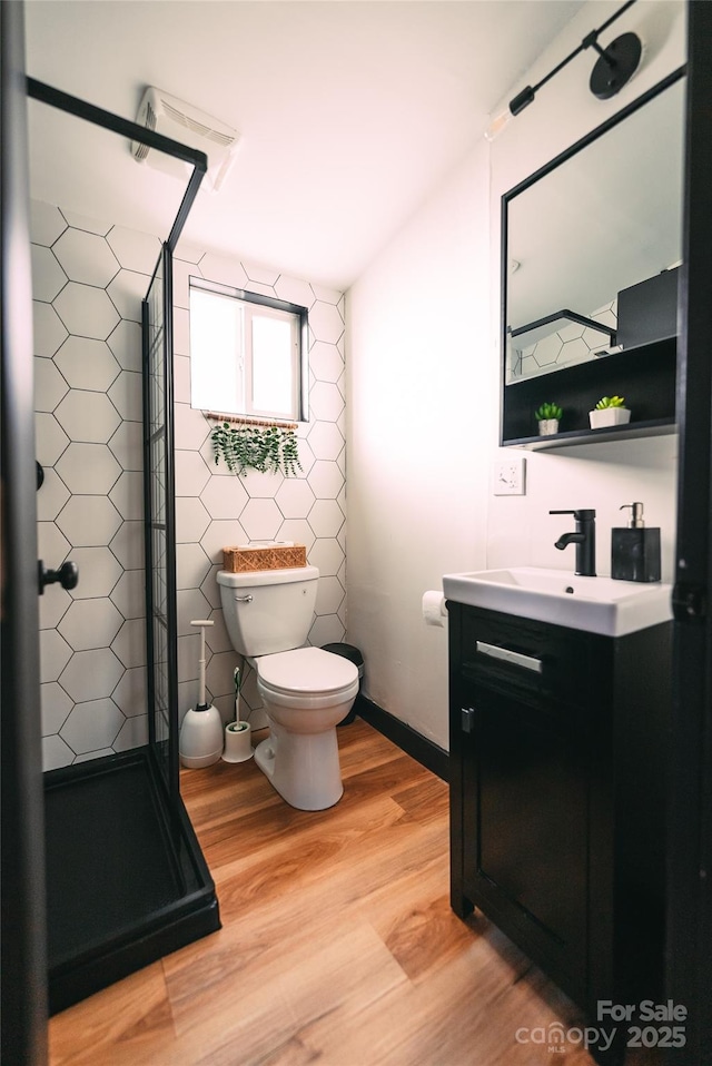 bathroom with toilet, hardwood / wood-style floors, a shower, tile walls, and vanity