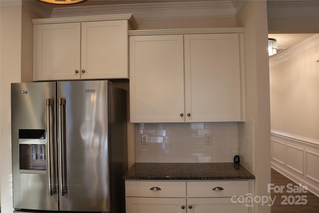 kitchen with high quality fridge, white cabinetry, dark stone countertops, decorative backsplash, and ornamental molding