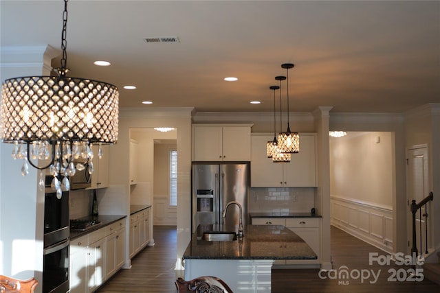 kitchen featuring an island with sink, stainless steel appliances, decorative light fixtures, dark stone counters, and sink