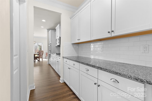 kitchen with white cabinetry, appliances with stainless steel finishes, ornamental molding, and dark stone countertops