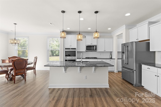 kitchen with sink, white cabinets, hanging light fixtures, stainless steel appliances, and a center island with sink