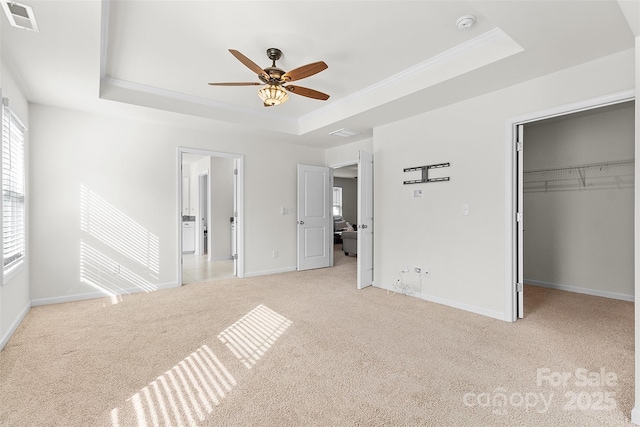 unfurnished bedroom featuring a walk in closet, light carpet, ornamental molding, a raised ceiling, and ceiling fan