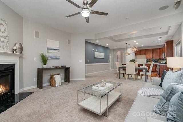 living room featuring ceiling fan, light colored carpet, and a raised ceiling