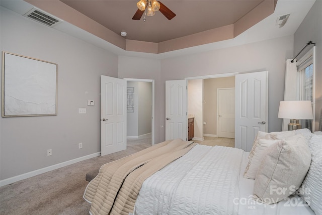 bedroom with ceiling fan, light colored carpet, connected bathroom, and a raised ceiling