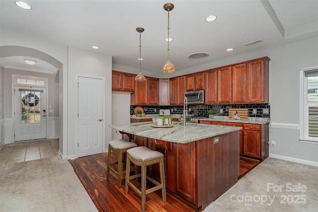 kitchen featuring light stone countertops, dark tile patterned flooring, decorative backsplash, pendant lighting, and an island with sink