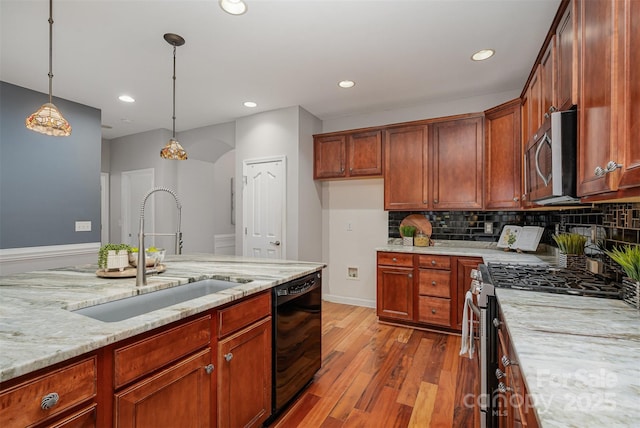 kitchen with pendant lighting, stainless steel appliances, sink, light wood-type flooring, and light stone counters