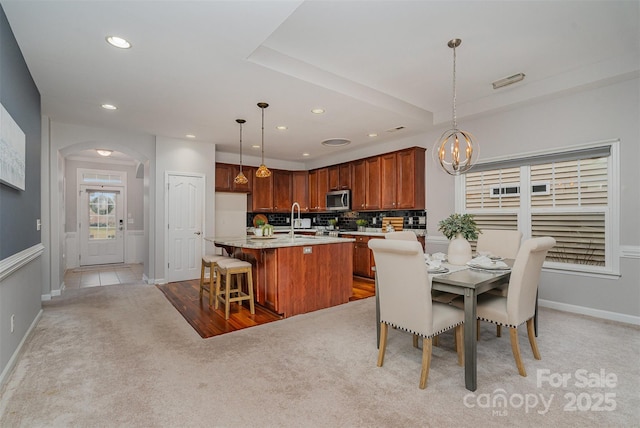 kitchen featuring sink, decorative light fixtures, a kitchen island with sink, and light carpet