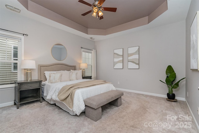 carpeted bedroom with ceiling fan and a tray ceiling