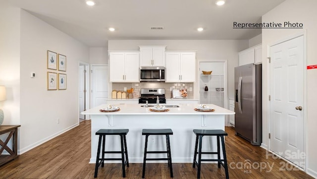 kitchen featuring white cabinets, stainless steel appliances, tasteful backsplash, an island with sink, and sink