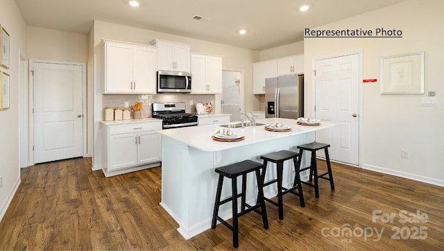 kitchen with a kitchen breakfast bar, appliances with stainless steel finishes, white cabinetry, and a kitchen island with sink