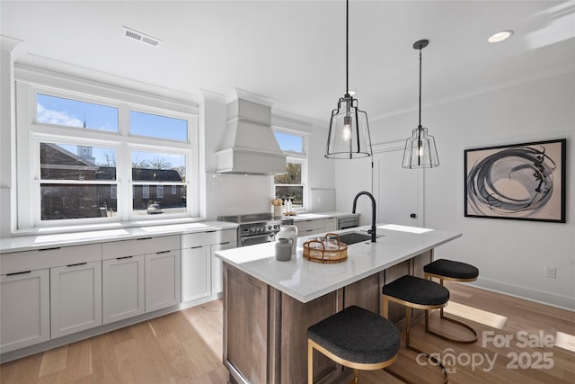 kitchen with decorative light fixtures, custom exhaust hood, high end stove, sink, and an island with sink