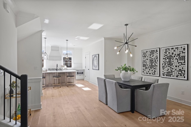 dining space featuring sink, light hardwood / wood-style flooring, ornamental molding, and a chandelier